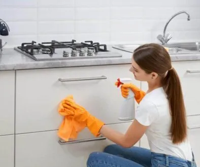 Sprzątanie Gdańsk, Gdynia, Sopot - Trójmiasto i okolice - Kobieta w pomarańczowych rękawiczkach demonstruje dbanie o kuchnię, używając spryskiwacza i ściereczki, aby uzyskać czystość kuchni, czyszcząc szufladę przy kuchence i zlewie.